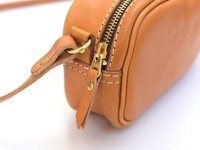 淺棕色皮革隨身單肩小包，金色 YKK 拉鍊，皮革肩帶連接處有金色卯釘和圓環。