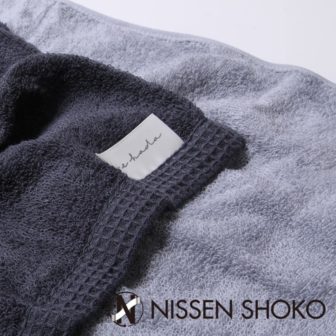 兩條不同深淺的灰色長毛巾，其中一條深灰色毛巾邊緣有格紋織法，並繡有「re hada」字樣的白色標籤。