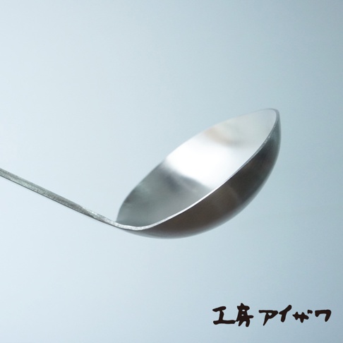 金屬光澤的不鏽鋼湯勺，勺頭呈圓弧形，勺柄細長，背景為淺藍色調。