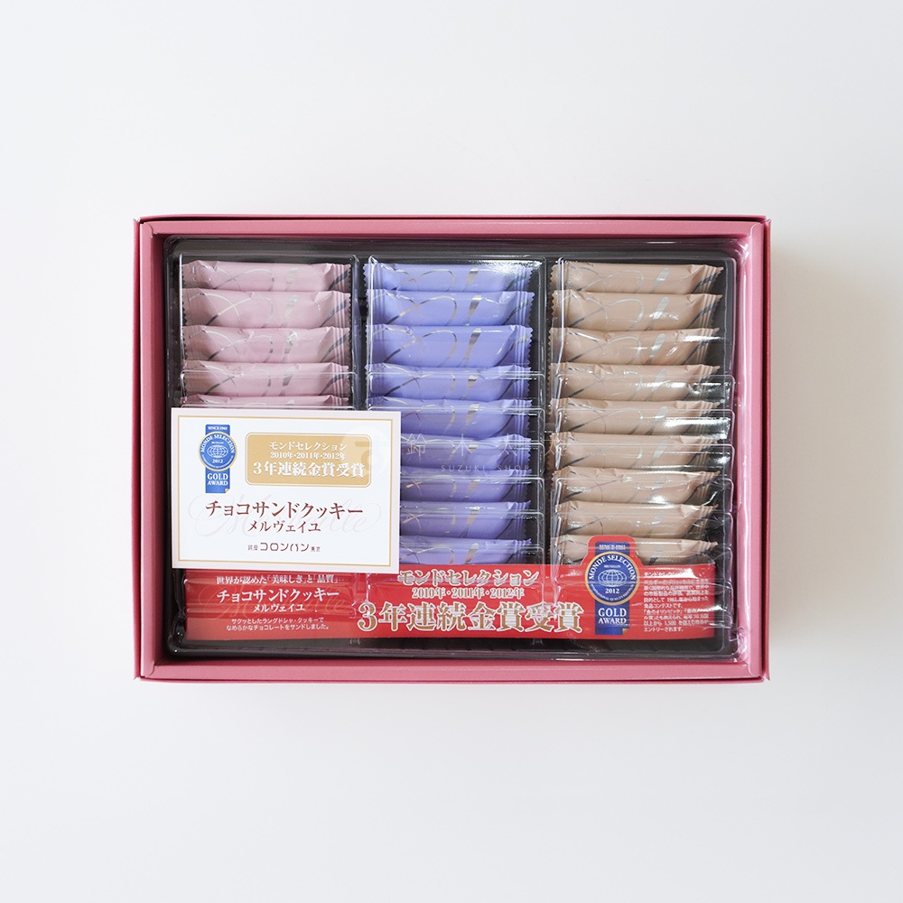 模式B： 粉紅色禮盒中裝有三層巧克力夾心餅乾，每層有九個獨立包裝的餅乾，顏色分別為淡粉色、淡紫色和米色，包裝上有金色壓紋。左側貼有獎牌和日文說明，右側也有獎牌和日文說明。
