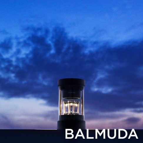 The Speaker 無線揚聲器，黑色底座和頂蓋，透明圓柱形外殼，內部裝置著數個發光的真空管，置於黃昏天空背景下的平台。