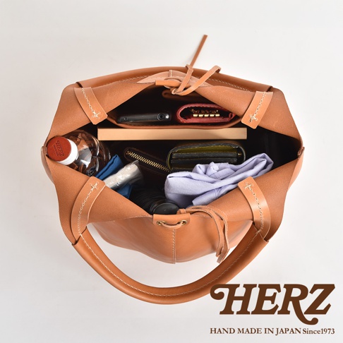 職人手作皮革球形肩掛托特包，焦糖棕色，內部裝有手機、錢包、鑰匙包、水瓶及衣物。
