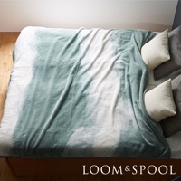 一張鋪在雙人床上的淺綠色與白色漸層印花短絨毯，質地柔軟，毯子上有明顯的絨毛紋理。