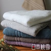 堆疊著五條今治飯店毛巾，顏色從上至下分別為白色、淺灰色、藍綠色、棕色和淡紫色。毛巾皆為純色，材質觸感柔軟，邊緣有細緻的羅紋裝飾。