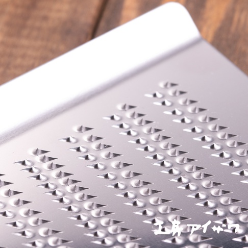 不鏽鋼磨泥器，表面有密集的菱形孔洞和凸起的磨齒，銀色金屬材質，部分區域反光。