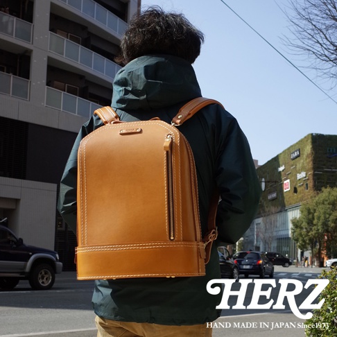 職人手作淺棕色皮革立體商務後背包，具有簡潔的方形輪廓，正面中央有一條垂直拉鍊，搭配對比色的縫線，展現細緻工藝。