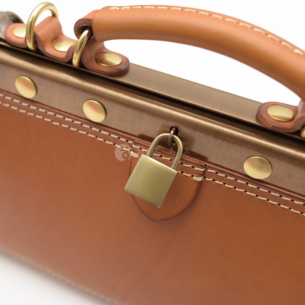 職人手作皮革復古口金兩用手提包，以咖啡色皮革製成，搭配復古銅色金屬鎖頭、釦飾及提把，縫線清晰，展現精緻工藝。