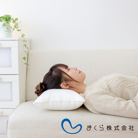 一名女子側臥在米白色沙發上，頭枕著一個白色蓬鬆的午睡枕。枕頭表面有縫線，材質看似柔軟。