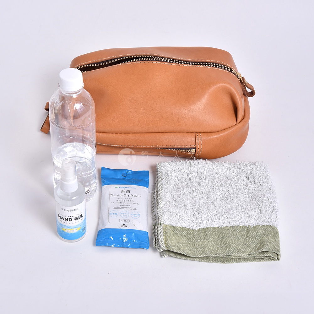 一個棕褐色皮革手提包，旁邊擺放著一瓶水、一包濕紙巾和一條淺綠色條紋毛巾