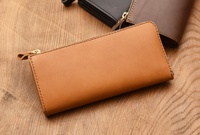 近距離拍攝職人手作皮革Organ雙拉鍊L型長夾，皮革呈現自然的棕褐色，搭配銀色拉鍊。右後方可見黑色及深棕色皮革長夾。