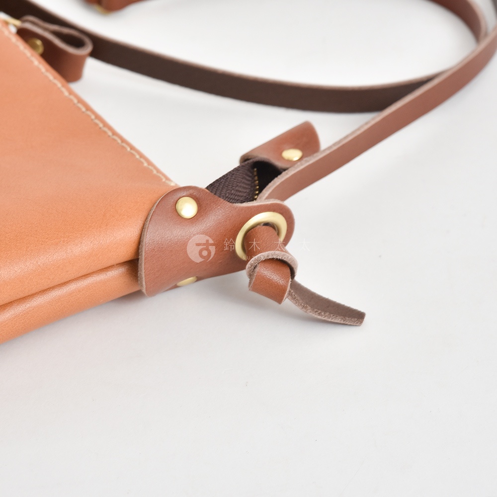 職人手作皮革直式隨身單肩包，展示焦糖棕色皮革細節，包含拉鍊、金屬扣環及皮革背帶。