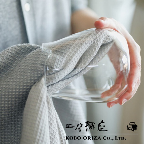 灰色棉麻混紡拭巾，具有鬆餅紋理，正被一隻手用來擦拭玻璃杯。