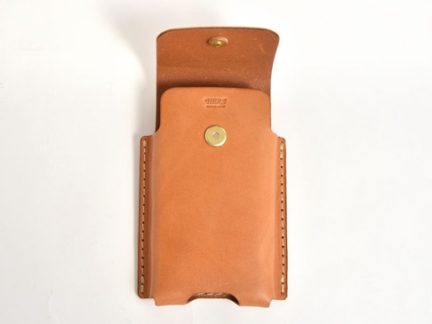 職人手作淺棕色皮革三用手機收納包，正面有金色金屬按扣，翻蓋處也有一個金色金屬按扣。包體側面有明顯的縫線。