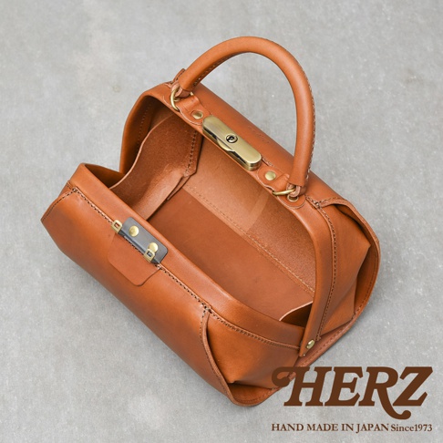 職人手作皮革Organ兩用口金手提包，呈現溫潤的棕褐色，材質為質感皮革，包身結構挺立，配有金色鎖扣與提把，風格簡約復古。