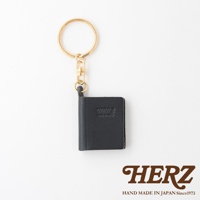 黑色皮革製成、書本造型的鑰匙圈，配有金色金屬環和扣環，皮革表面壓印有「HERZ」品牌標誌。