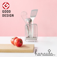 不鏽鋼筷籠內有打蛋器、湯勺和鍋鏟，置於桌面上，左側有兩顆番茄置於木質砧板上。