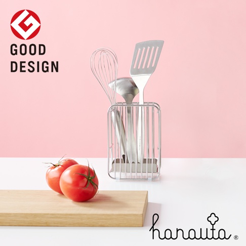 不鏽鋼筷籠內有打蛋器、湯勺和鍋鏟，置於桌面上，左側有兩顆番茄置於木質砧板上。