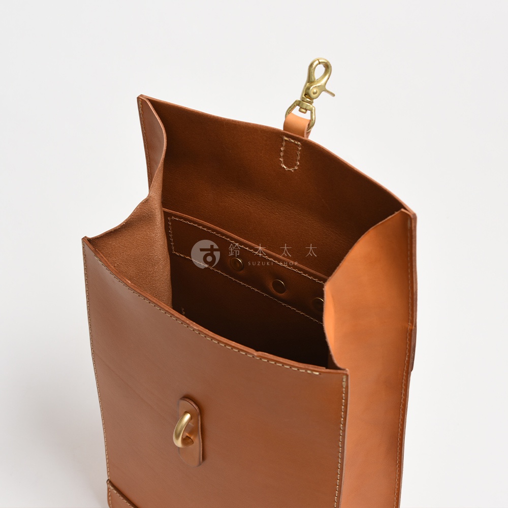 職人手作皮革紙袋風後背包，呈現經典棕色，材質為真皮。包款開口設計，內部有隔層，並搭配黃銅色金屬扣環與掛鉤。
