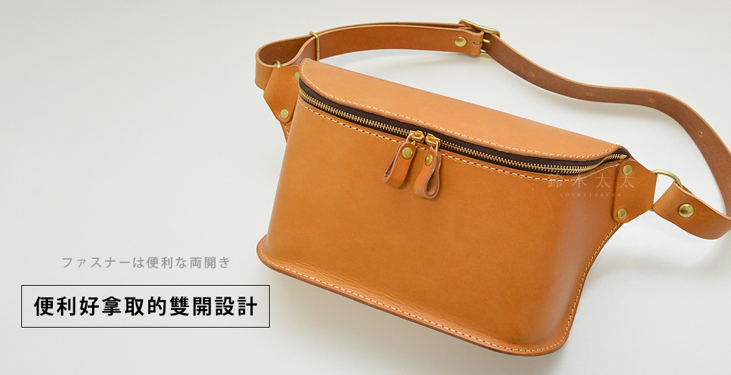 職人手作立體斜背包，採用淺棕色皮革製成，設有雙拉鍊開口，搭配可調節的皮革長背帶及金屬扣環。