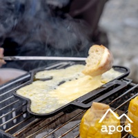 黑色鑄鐵熱壓三明治烤夾，正在烤製融化的起司和一塊麵包，旁邊還有玉米。