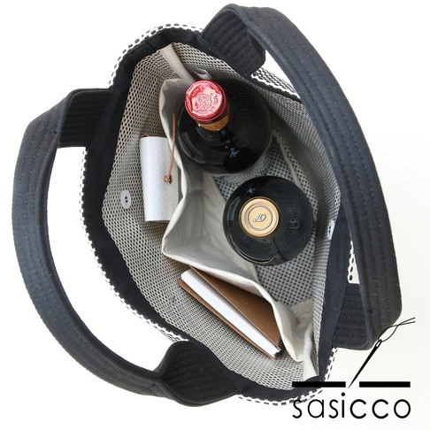 三河木綿刺子織直式收納托特包，黑色提把，包內有兩瓶深色玻璃瓶裝物、一個白色小捲筒物品和一本褐色封面的筆記本，包內襯為網格狀織紋。