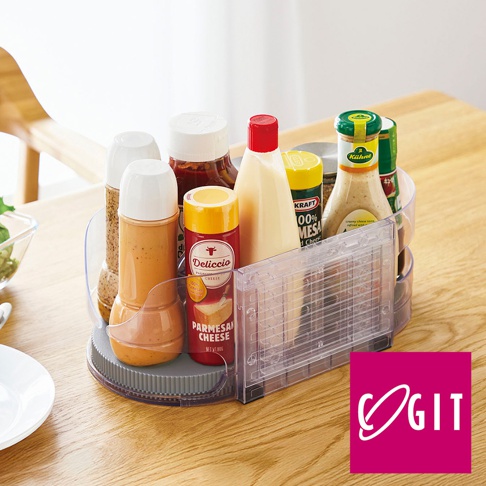 透明壓克力材質的橢圓形旋轉收納盤，盤內裝有各式調味品瓶，包括番茄醬、沙拉醬、香料粉、起司粉等，產品置於木製桌面。