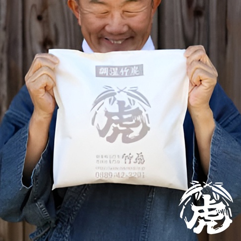 一個男人拿著一個白色袋子，上面印有灰色日文文字和一個虎形圖案。袋子上有「調濕孟宗竹炭」字樣。