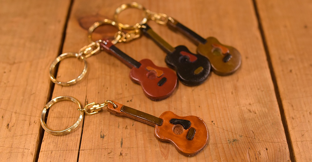 四個職人手作皮革吉他造型鑰匙圈，包含棕色、紅色、黑色及深棕色，搭配金色鑰匙圈，精緻可愛。