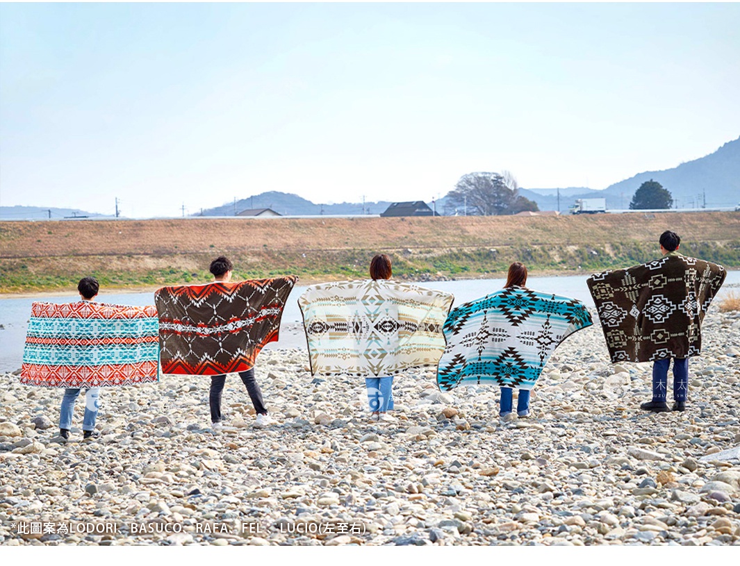 五位人士在河岸邊展示四款異國民族風毛巾毯。毛巾毯設計包含幾何圖案，顏色有藍色、白色、棕色及橘色。