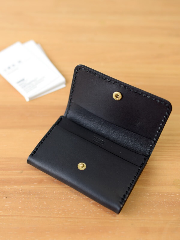 黑色皮革名片夾，以手工縫線製作，內有金屬按扣，可收納名片。