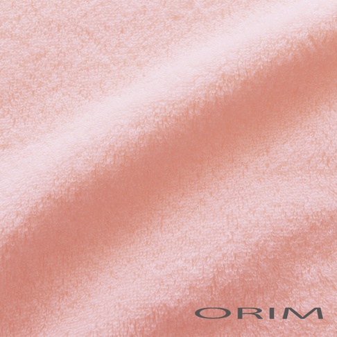 這是一張 ORIM 品牌的粉色毛巾近距離特寫影像，展示了毛巾柔軟細緻的純棉纖維紋理，表面呈現蓬鬆且帶有光澤的毛圈質感，右下角印有淺灰色的 ORIM 品牌標誌。