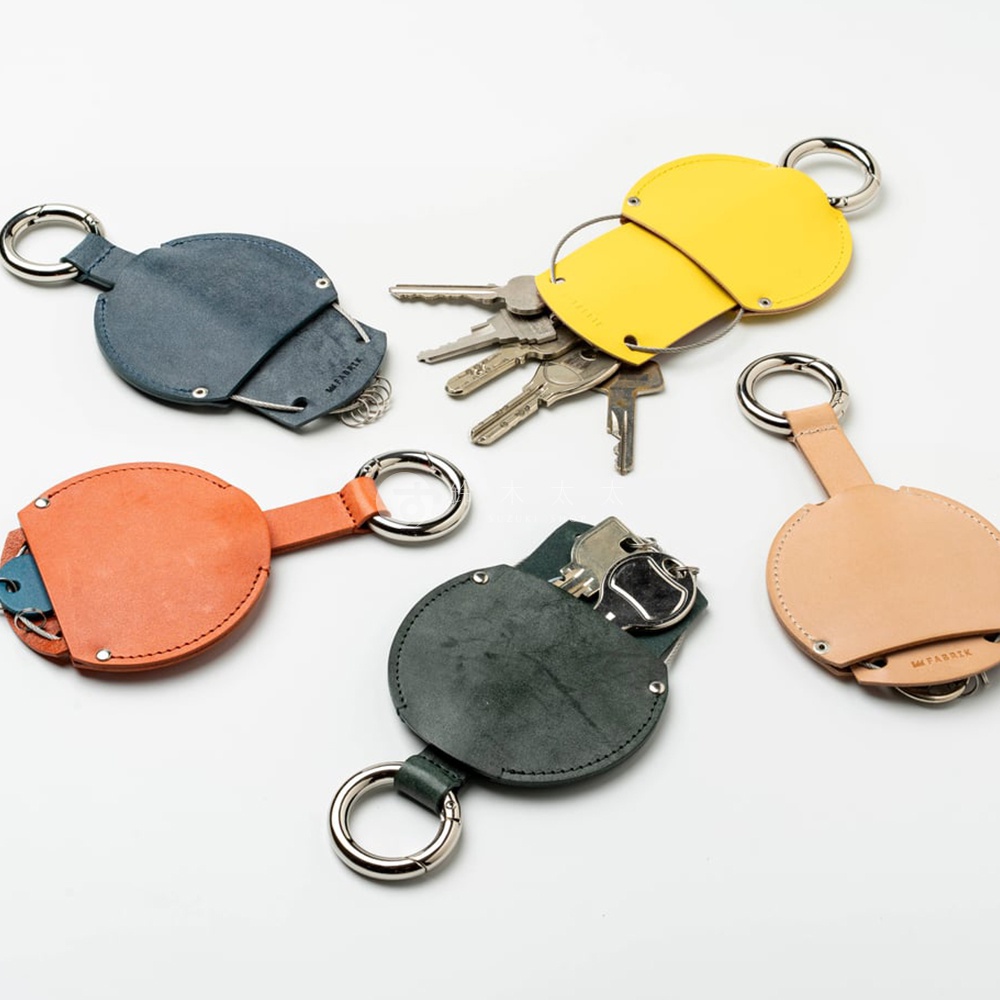 FABRIK 皮革圓形收納鑰匙圈，展示了四款不同顏色的設計，包括深藍色、橘紅色、墨綠色和黃色，鑰匙收納包內可見金屬鑰匙，鑰匙圈與收納包以皮革連結。
