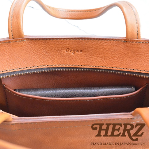HERZ 職人手作皮革托特包內部，可見拉鍊開口、側面口袋及一個深色長夾。