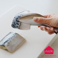 一隻手拿著銀色金屬材質的不沾桌調理幫手夾，夾著一塊帶有魚皮和魚肉紋路的鯖魚塊。另一塊鯖魚塊放在白色紋理的砧板上。