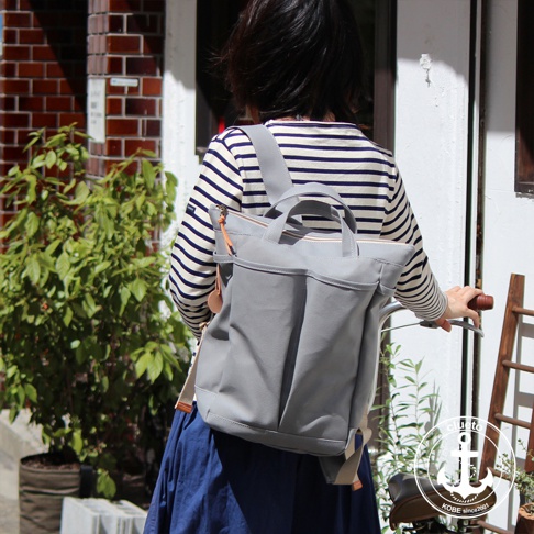 灰色高島帆布後背包，設有雙提把、拉鍊開口和前置口袋。