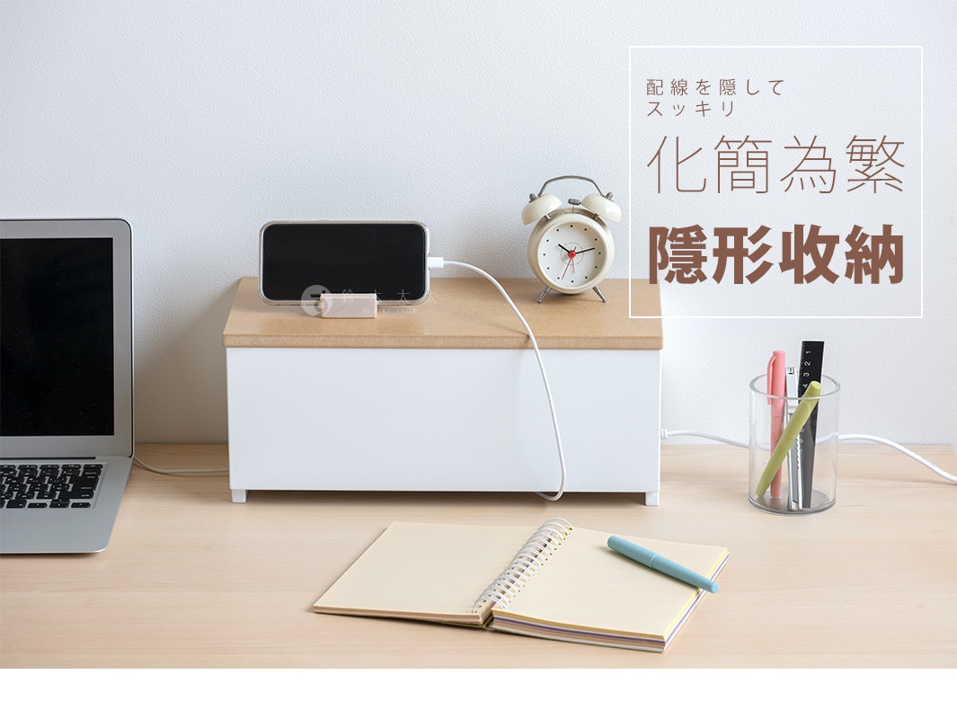 白色木藝附蓋電線收納盒，頂部為淺木色，盒身前方有電源線通過。旁邊擺放著一台筆記型電腦、一個復古鬧鐘、一本筆記本和一個透明筆筒，筆筒內有三支筆。