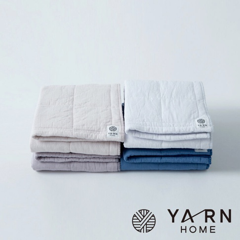 堆疊的UKIHA格紋毛巾，左側為米白色和淺紫色，右側為白色和靛藍色，皆有縫線格紋和品牌標籤。