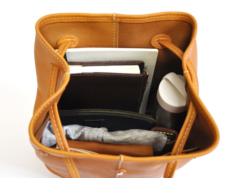 職人手作皮革可調式兩用大容量托特包，內有筆記本、皮夾、帆布袋和保溫瓶，包款為卡其棕色，搭配白色縫線，簡約實用。