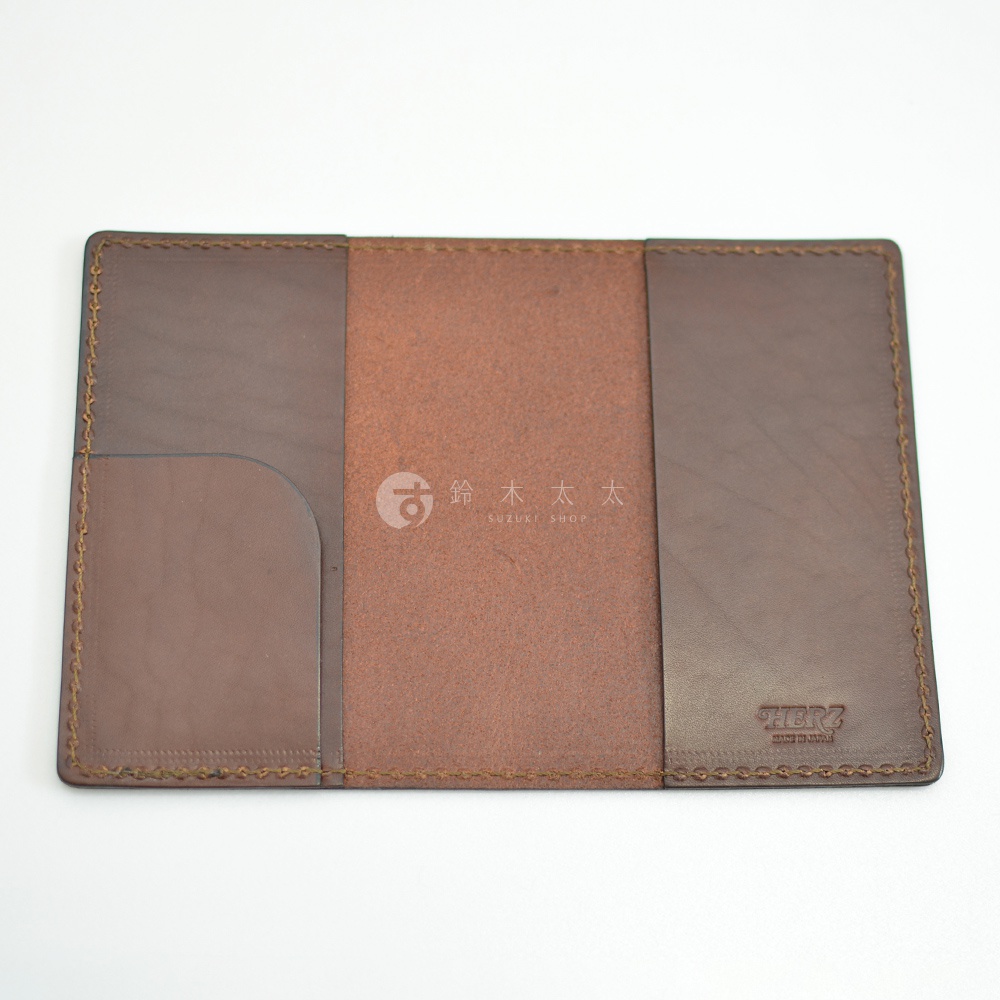 深棕色皮革護照套，內部設計有左右兩側插槽，中間為麂皮材質，右側角落壓印有「HERZ」品牌標誌。