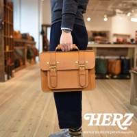 職人手作皮革經典雙扣兩用單肩包，材質為天然牛皮，顏色為淺棕色，包款設計簡約，有雙扣和提把，可肩背或手提。