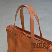 職人手作的棕色皮革肩背拉鍊托特包，包身線條簡潔，搭配金屬拉鍊與手挽帶，展現經典質感。