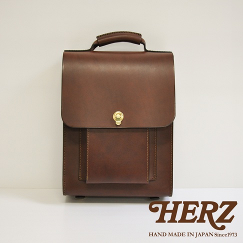 職人手作皮革復古後背包，採用光滑的咖啡色皮革，配有金色扣環和前置收納袋，整體設計簡潔耐用。