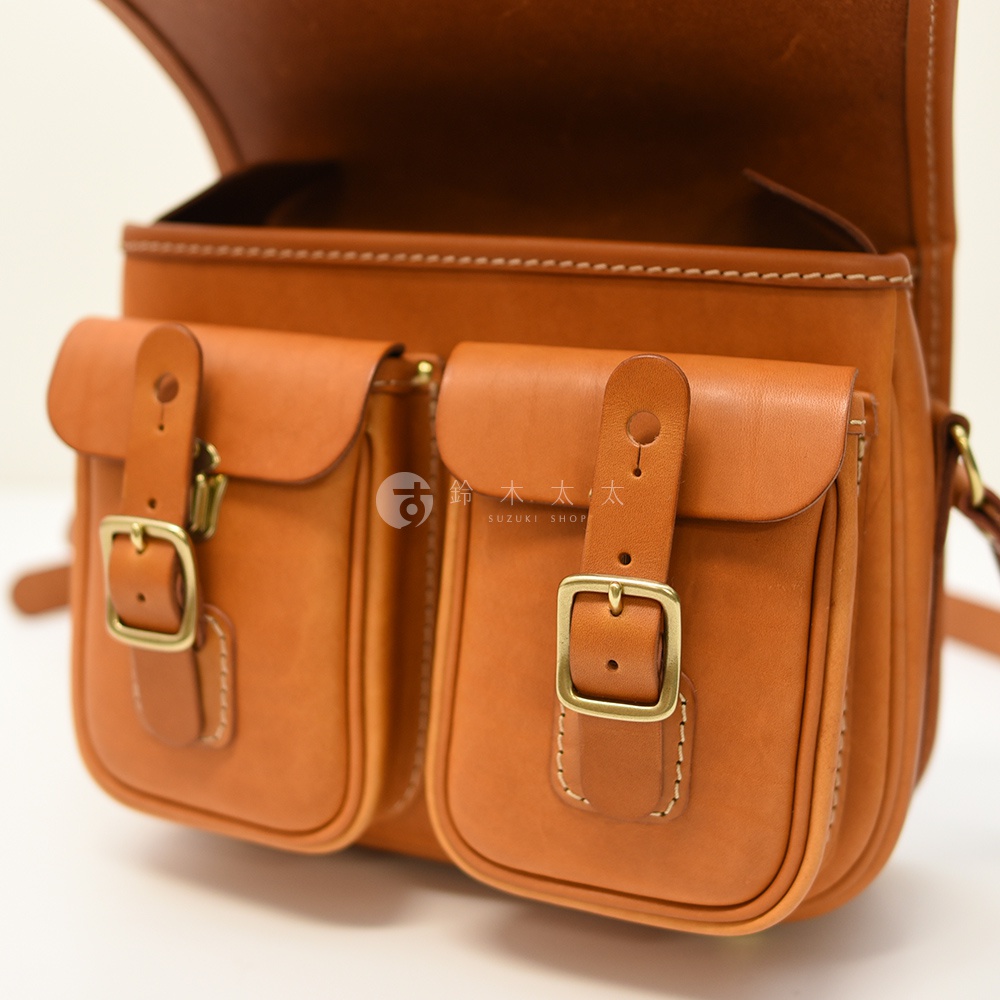 日本HERZ 職人手作皮革經典雙扣郵差包 CK-100，以其精湛的工藝和耐用的材質，展現出復古的魅力。包包採用高品質皮革製作，顏色溫潤，表面帶有自然的紋理。雙扣設計不僅美觀，也方便開合，兩個前袋提供了額外的收納空間，整體造型經典實用，適合各種場合攜帶。