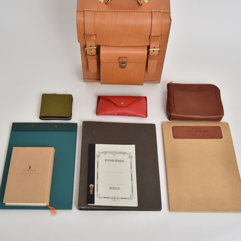 皮革後背包、綠色皮革零錢包、紅色皮革筆夾、棕色皮革手拿包、綠色文件夾、兩本筆記本，以及一個淺棕色文件夾。