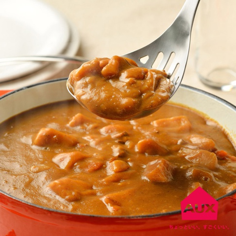 不鏽鋼濾湯火鍋杓盛起一勺濃稠的咖哩燉菜，鍋內是滿滿的紅蘿蔔塊與肉塊，湯頭呈金黃色。