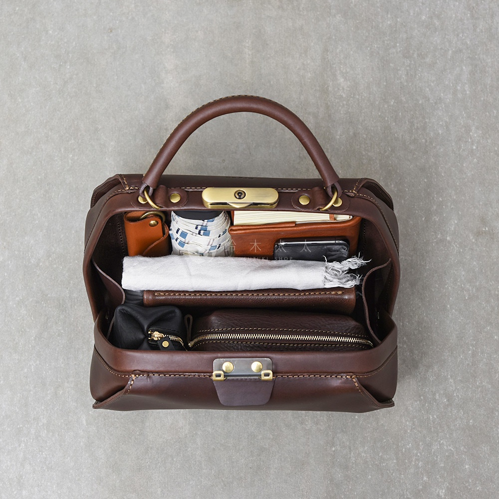 深棕色皮革手提包，內部裝有筆記本、錢包、折疊傘、毛巾和化妝包。包包配有金色口金鎖和手提把。