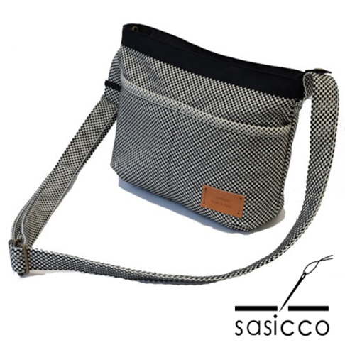 黑白格紋三河木綿刺子織斜背包，搭配黑色包邊與皮革品牌標籤，斜背帶可調節。