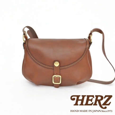 HERZ 職人手作復古棕色皮革斜背包，搭配金色釦環和縫線細節，標有「HAND MADE IN JAPAN Since1973」字樣