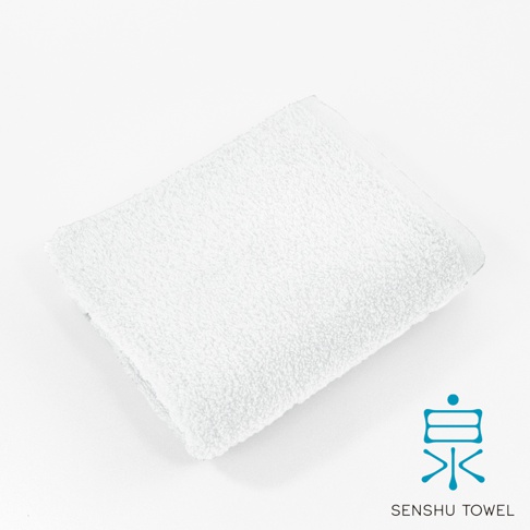 一條白色的長纖毛巾，材質蓬鬆柔軟，邊緣有精緻的包邊，右下角有藍色的「泉」字 Logo 和「SENSHU TOWEL」字樣。