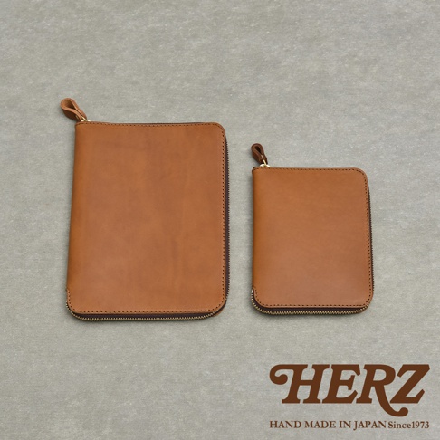 兩個棕色皮革記事本收納包，一個較大一個較小，皆有拉鍊開合，底部印有HERZ HAND MADE IN JAPAN Since1973字樣